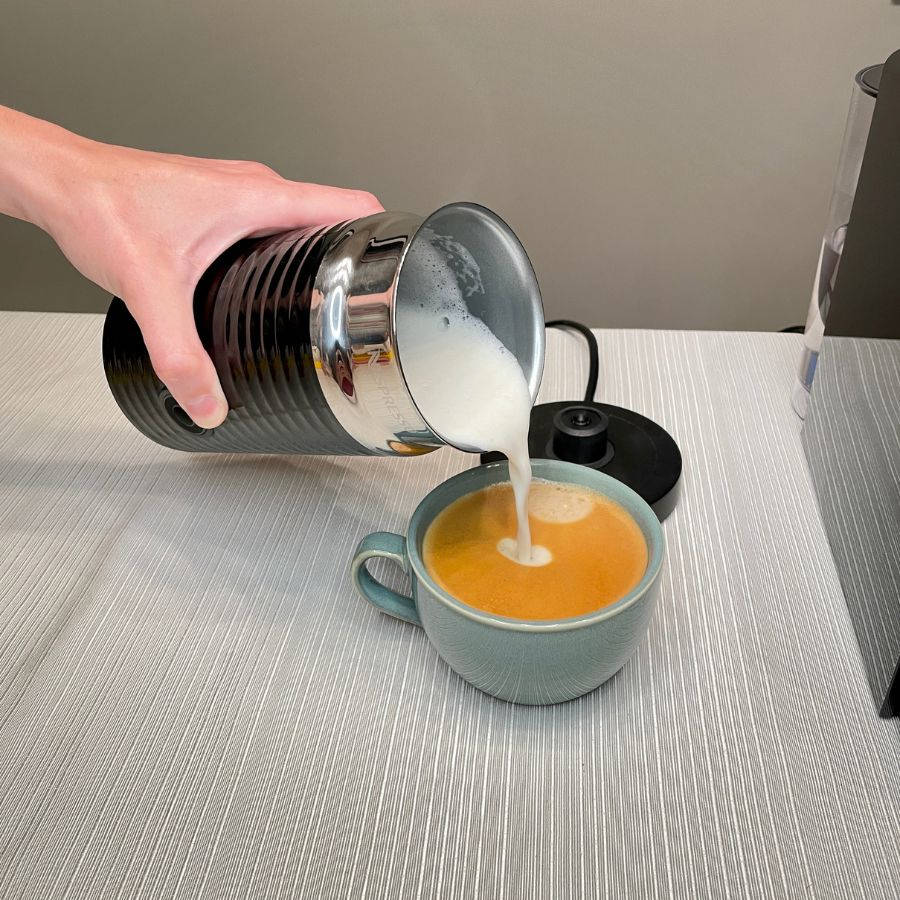 pouring the frothed milk into the coffee using a Nespresso Aeroccino 3